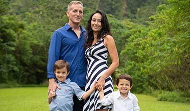 Family portrait of a dad, mom and two young boys in a lush green setting.