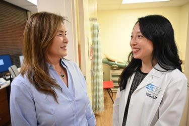 a female doctor and nurse talk stand in front of an exam room in a medical clinic.