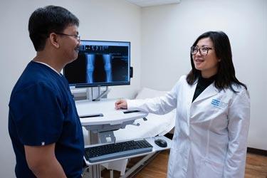 a female doctor and male medical assistant review an X-ray of a knee in an exam room.