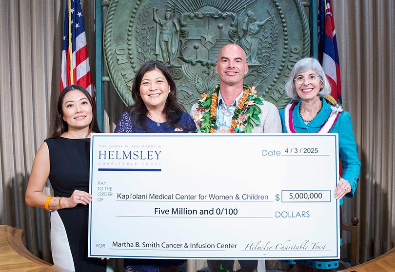 Four people holding a giant check for $5 million in front of the Hawaii state seal.