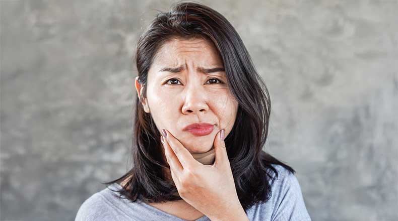 Woman holding her jaw with a concerned look on her face.