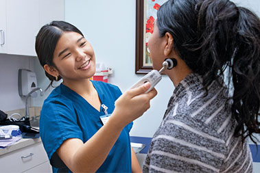 Smiling MA in blue scrubs with a patient in a clinic exam room.