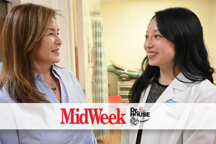 A female doctor and nurse talk to each other in front of an exam room in a clinic.