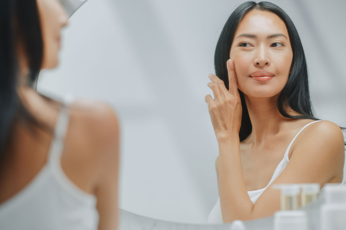 a beautiful older woman looks at her reflection in the mirror and applies face cream to her skin