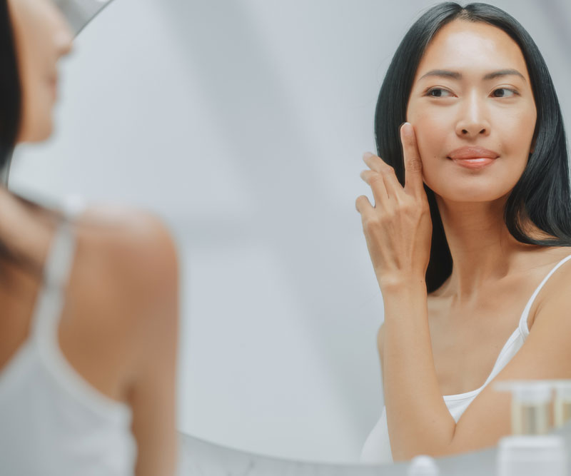 a beautiful older woman looks at her reflection in the mirror and applies face cream to her skin