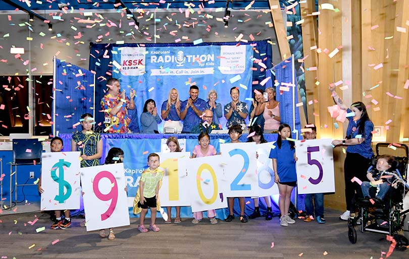 Children holding numbers showing $910,285 with confetti falling down and adults cheering.