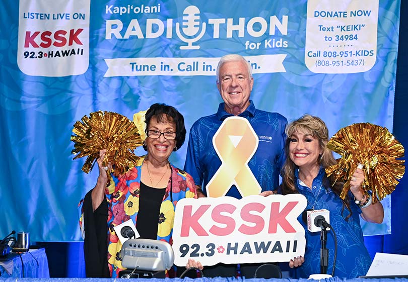 Radio personalities one man holding a sign for station KSSK, with two women holding pom poms.