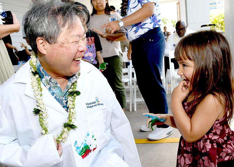 Doctor in white coat laughing as young girl puts a paint handprint on his coat.
