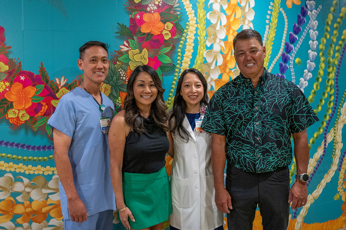 two men and two women stand in front of a wall mural of Hawaiian flowers