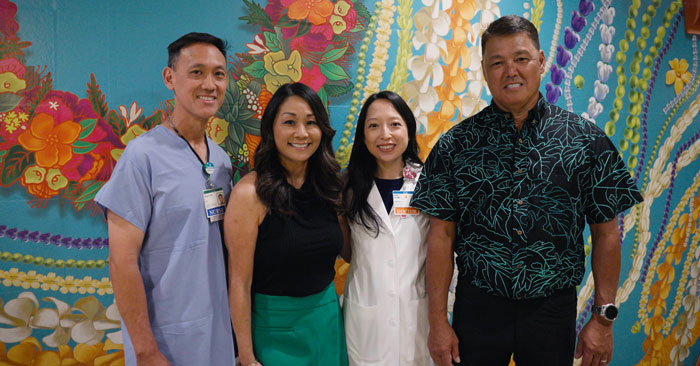 two men and two women stand in front of a wall mural of Hawaiian flowers