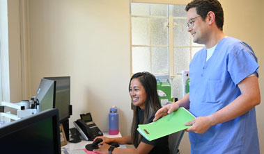 A doctor stands and looks at a computer with a program coordinator who is seated in front of the screen