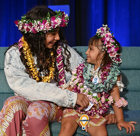 Two sisters smiling at each other, both wearing lei.