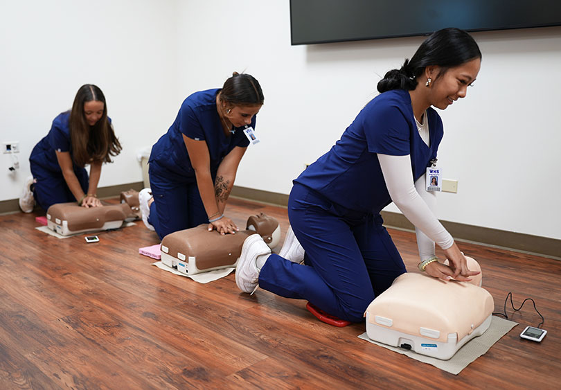 Students wearing scrubs practice CPR on dummies.