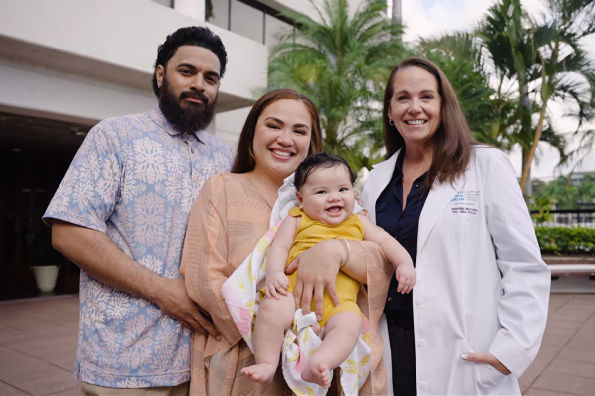 a dad and mom hold their baby girl and stand with a doctor smiling in the courtyard at Pali Momi Medical Center