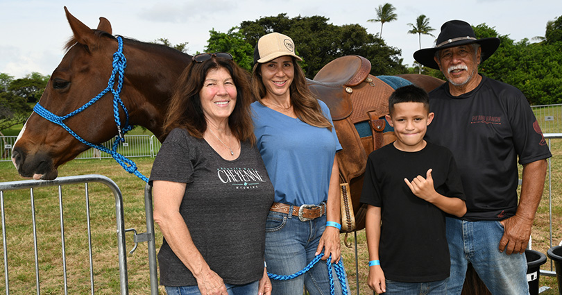 Local family standing beside a horse with one person holding the reigns and young boy throwing a shaka.