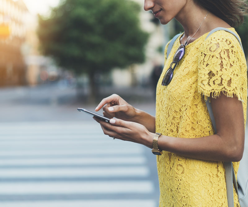 a women walking towards crossroads holding her mobile phone